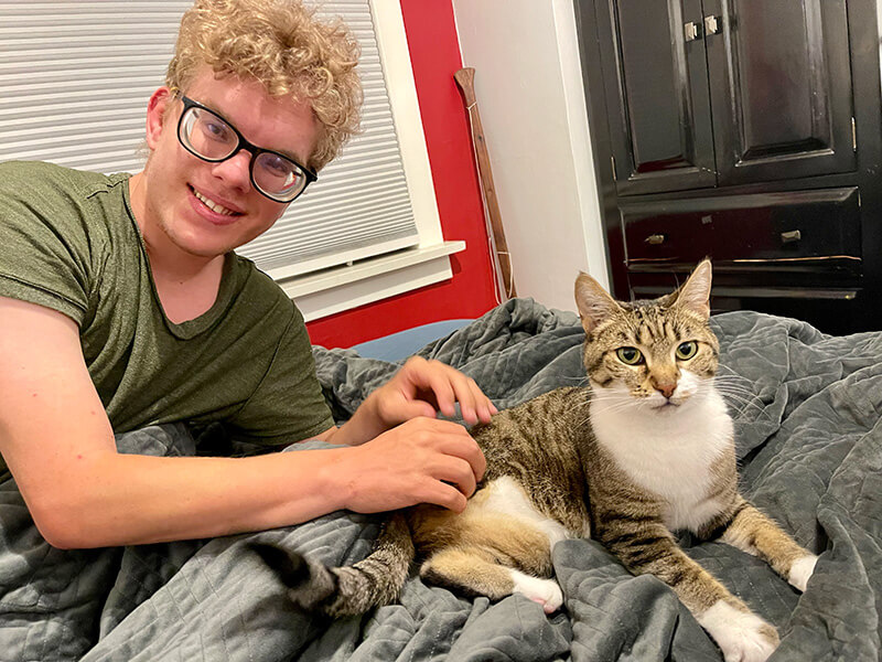 Scott sitting with his new cat, Jiffy. She is a grey tabby with three legs.