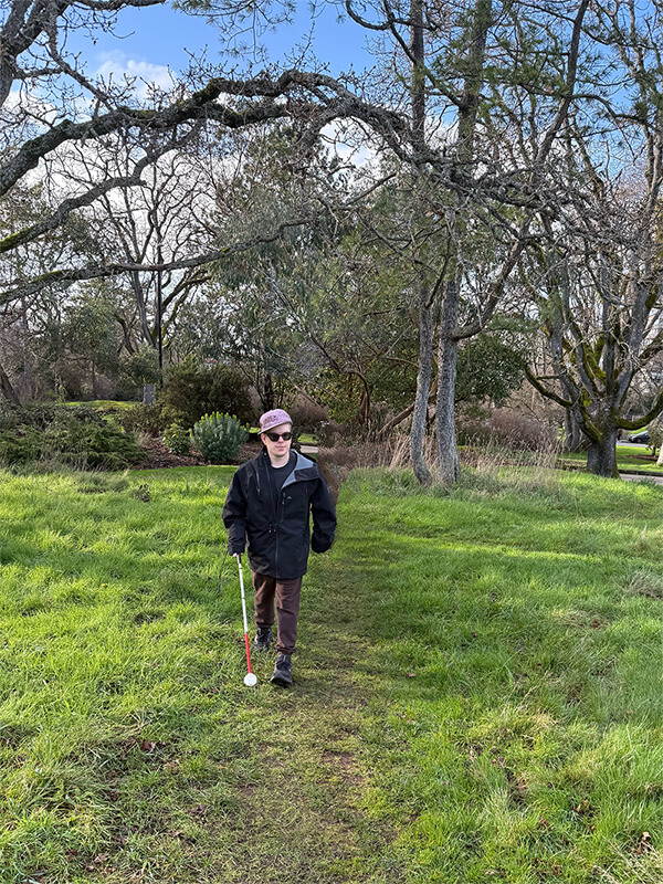 Scott walking with his cane on a park trail on a sunny day.